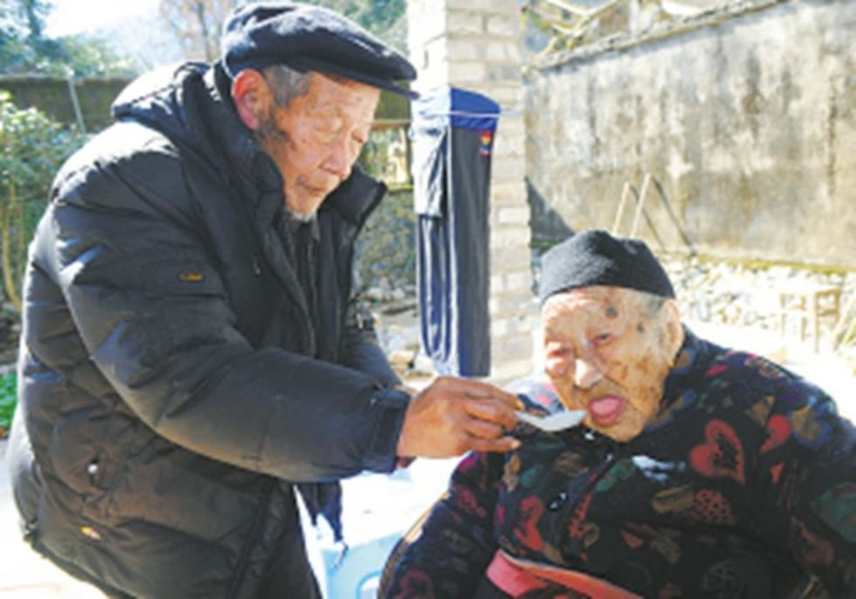 　　照顾老人的大儿子何国豪今年也已经91岁，身体也很健朗，偶尔甚至还能上山去砍柴。母子两人同时成为老寿星，进入了村里的名人录。老人所在的河洪村，环境很好，青山环绕，绿水穿村，空气清新。
