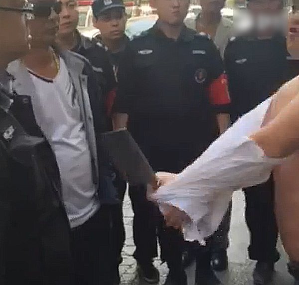 4月19日上午9时许，王国强的中队与淮河路办事处的工作人员一起，上街清理辖区内占道经营的摊贩。清理到汉江路与嵩山路交叉口东北角一家胡辣汤店时，发现该店在门前的人行道上，摆了一些桌凳和灯箱。执法人员上前清理占道物品时，一名光头、体型较胖的男子掂着一把菜刀，从店里冲了出来，对着执法人员大声叫骂。他上前制止，被对方指着鼻子辱骂和威胁。图为男子持刀脱衣。