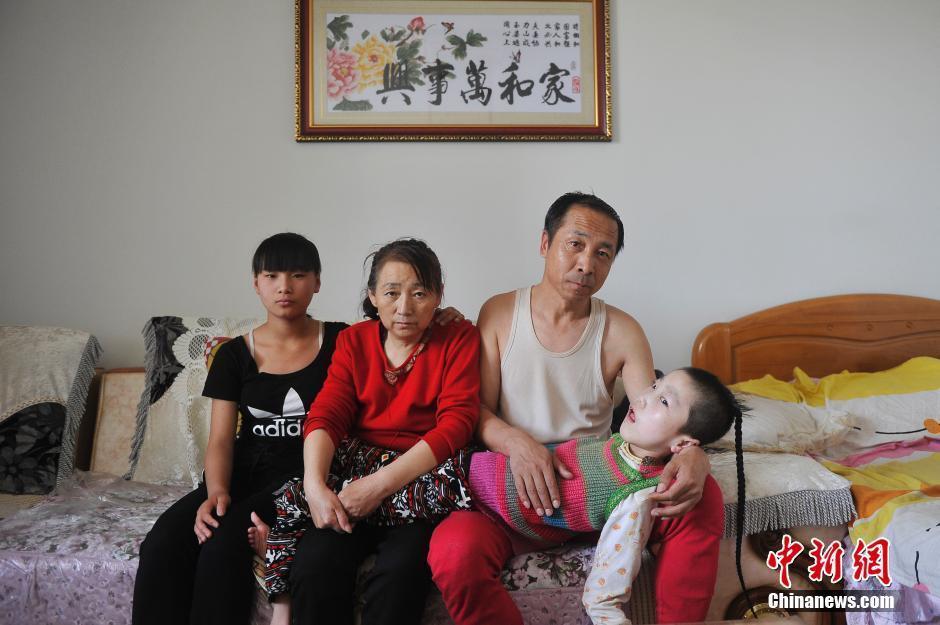 　　小丽坤属于重度脑瘫，只能躺在床上，手脚不能正常运动，也没有语言功能，连咀嚼吞咽的功能都不具备。因此，李焕梅和丈夫赵玉春只能一人出去打工，另一人在家全天候照顾脑瘫养女。图为5月30日，赵玉春与妻子李焕梅、小女儿赵彬、脑瘫养女赵丽坤在家中拍摄全家福。