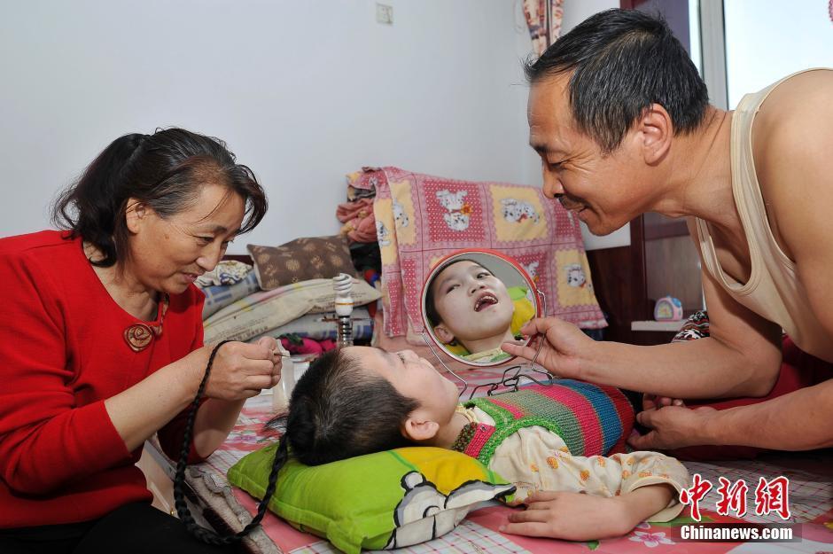 　　李焕梅患病后，家里的重担全部落在丈夫赵玉春身上，没有任何经济来源的她们全靠亲戚救助。李焕梅说，由于当年没有办理收养手续，致使小丽坤一直未能落户。她现在最大的愿望就是给孩子上个户口，这样小丽坤就能申请低保和残疾人补助。“孩子如果能安顿好，我就没有后顾之忧了。”李焕梅说。图为5月30日，赵丽坤起床后，养母李焕梅为女儿编辫子，养父赵玉春照镜子给她看。