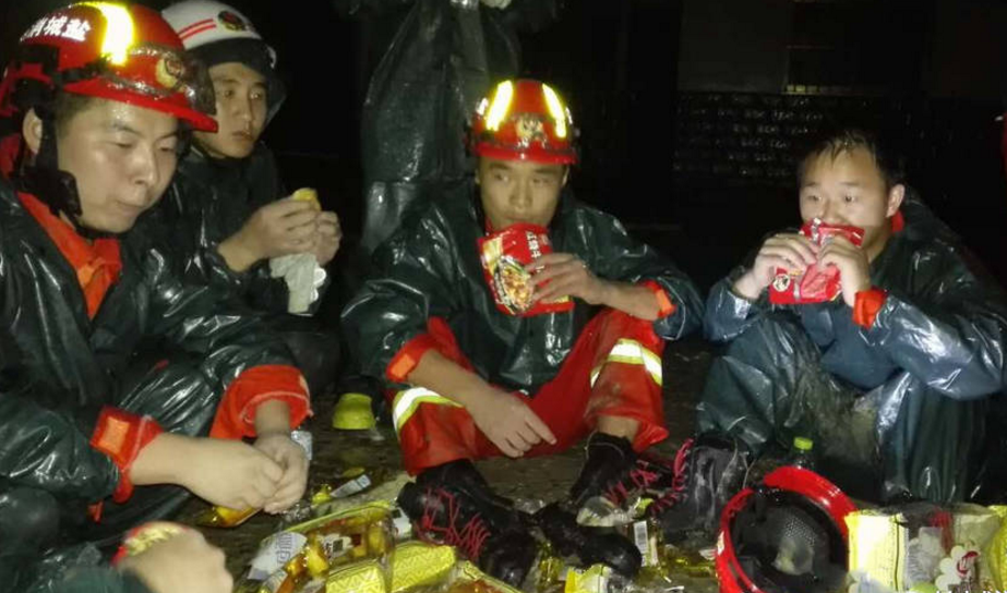 　　24日凌晨，参与救援达10小时的消防人员换防休息，坐在地上干嚼方便面补充能量。