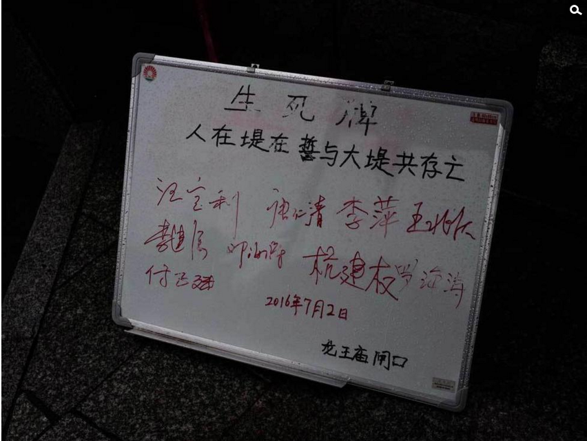 　　7月6日，武汉市遭遇特大暴雨袭击，长江水位超过28米，防汛形势极其严峻。位于两江交汇地的龙王庙码头一直以来都是武汉防汛的重中之重，记者在6日前往龙王庙码头附近探访时发现，沿江大道停满了各种渣土车，这些渣土车是用来运送防汛物资的。在马路边甚至堆放了各种防汛用的物品，比如黄沙、石子儿等等。图为武汉龙王庙码头立起防汛生死牌。