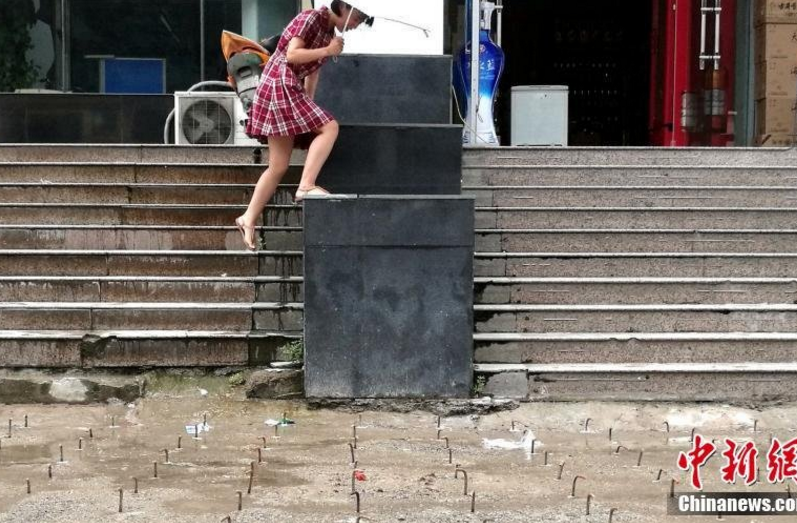 　　记者经调查了解，当地为了农业路快速通道项目，将该广场规划成了一条行车通道。因此处广场下方系大厦的两层地下停车库，钢勾则是为了下一步的道路加固所用。图为一名在此大厦办公的员工跳上台阶躲避钢勾。