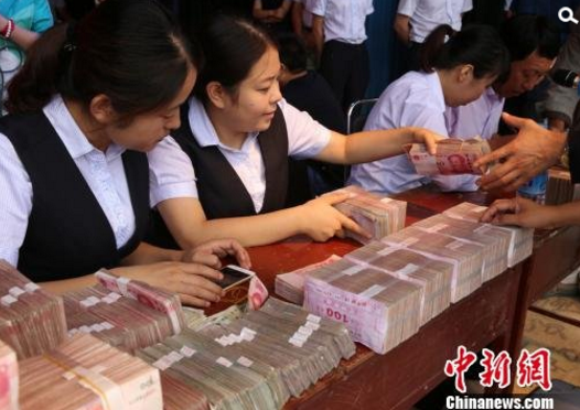 　　边国胜介绍，机场村人多地少，农民多年来以种菜为主，耗费劳力，收入甚微。“在种树之前我们做了调研，条件最好的村民家里存款也不超过10万元。3年前，边国胜探索采取“农户出地、出人，公司提供树苗、保证销售”的“零风险”模式，吸引农户参与苗木产业。公司为每户农户免费提供40万株云杉苗木，农户负责田间管理，3年后，农户将苗木全部交给公司，考虑到苗木的成活率，上交苗木不得少于38万株，则按照合同协议，每户分红30万元。这3年期间，公司每月还为每户农户发放1000元管护费。图为银行工作人员点钞。