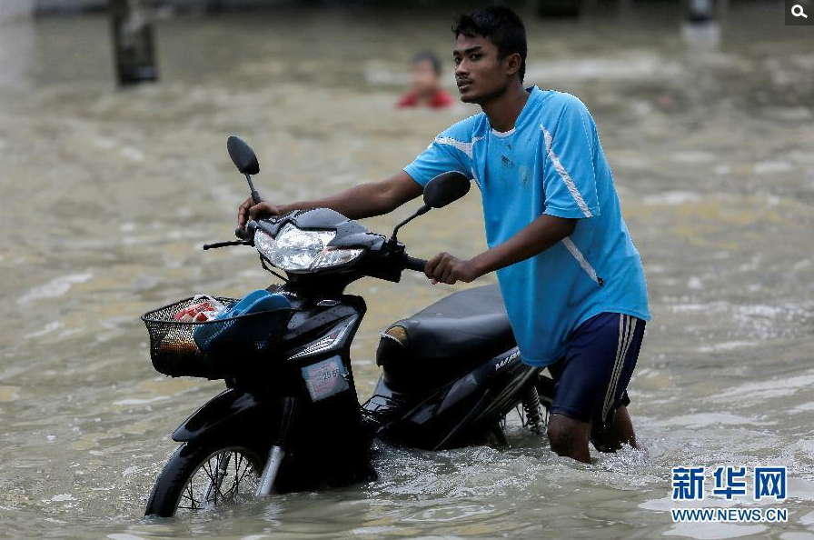 1月6日，在泰国南部受灾最严重的那空是贪玛叻府，一名男子推着摩托车涉水而行。新