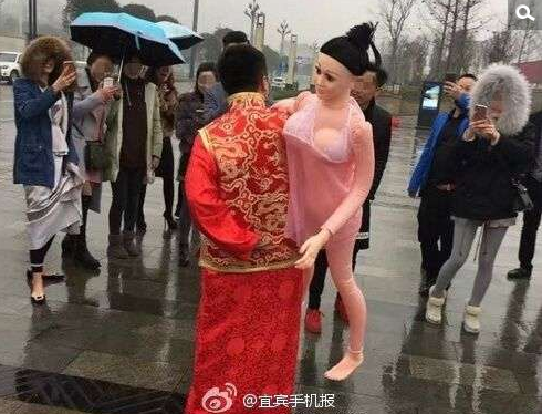 　　2月6日上午，在宜宾市翠屏区南岸长江之歌公园那里，一个20多岁的男的，穿一身古典的新郎装，冒着绵绵的细雨，背着他心爱的充气娃娃在水幕电影旁漫步。